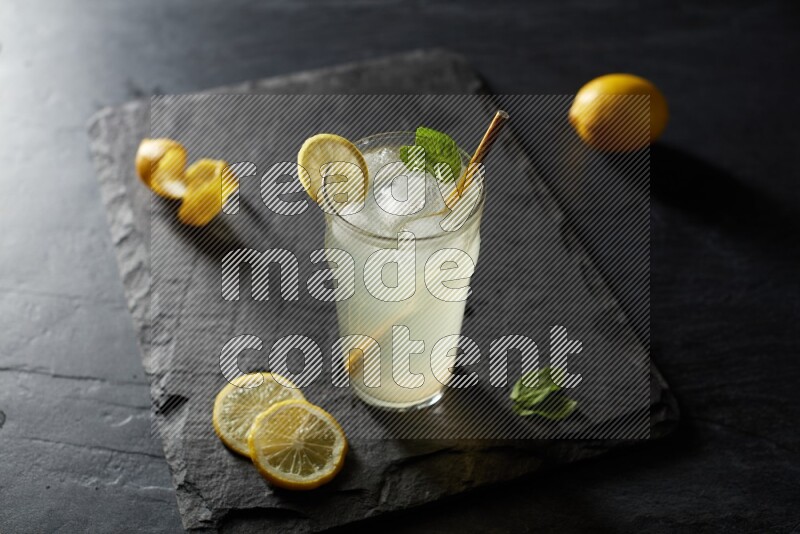 A glass of lemon juice with a straw on black background
