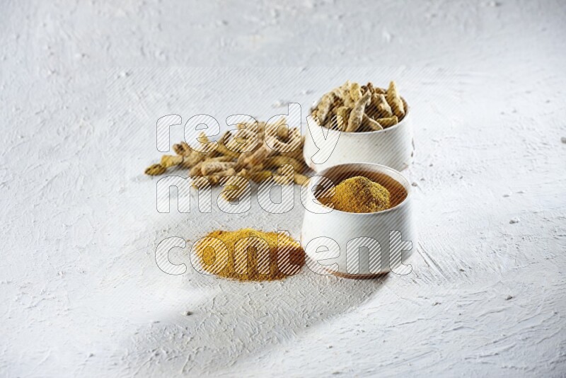 2 beige pottery bowls full of turmeric powder and dried turmeric whole fingers with powder and fingers next of it textured white flooring