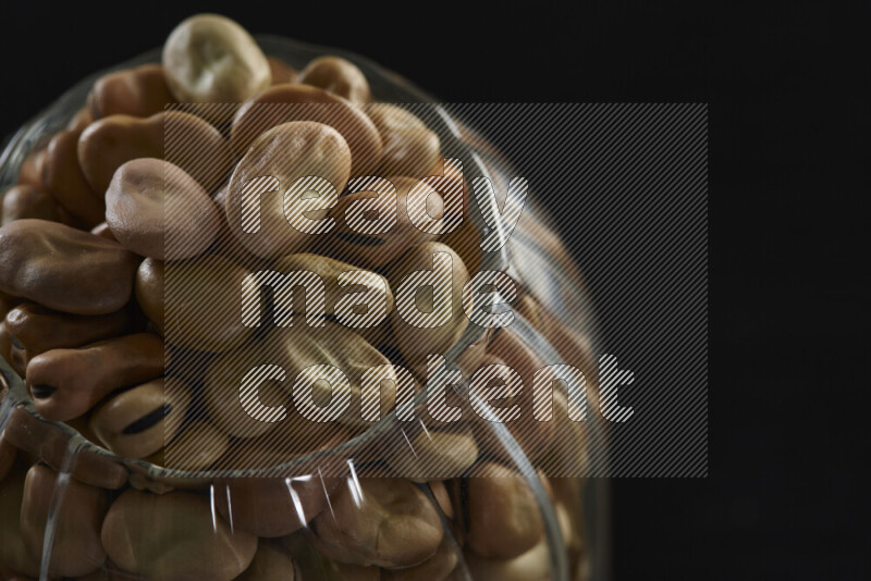 Fava beans in a glass jar on black background