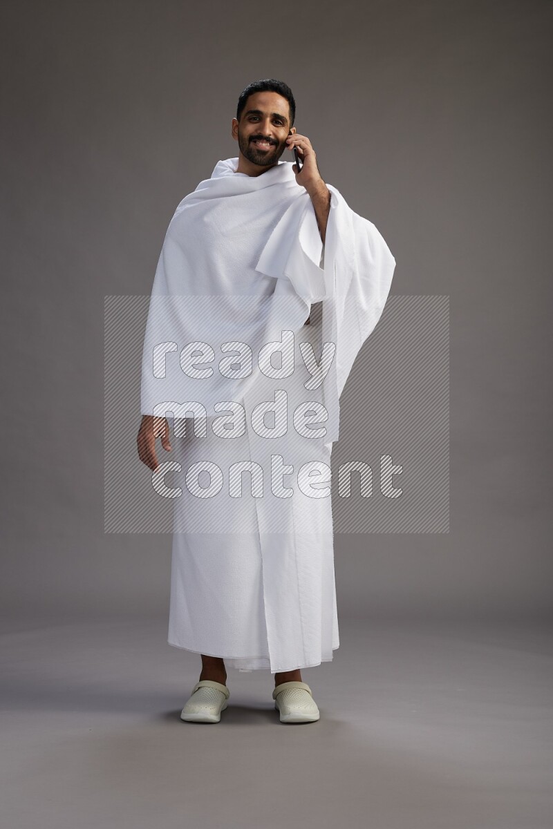 A man wearing Ehram Standing talking on phone on gray background