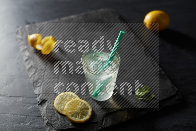 A glass of lemon juice with a straw on black background