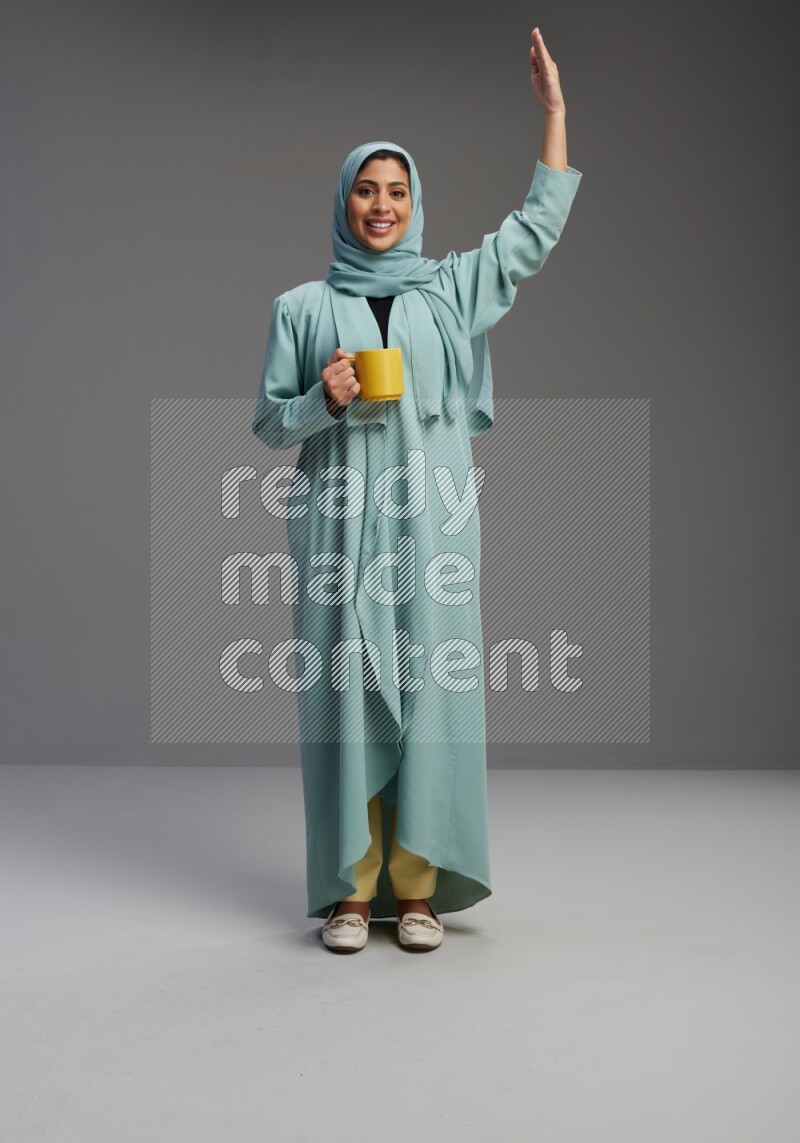 Saudi Woman wearing Abaya standing  holding a mug on Gray background