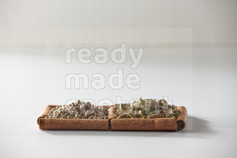 مربعان من أعواد القرفة ممتلئان بحبوب الهيل وحبوب الفلفل الأبيض علي خلفية بيضاء