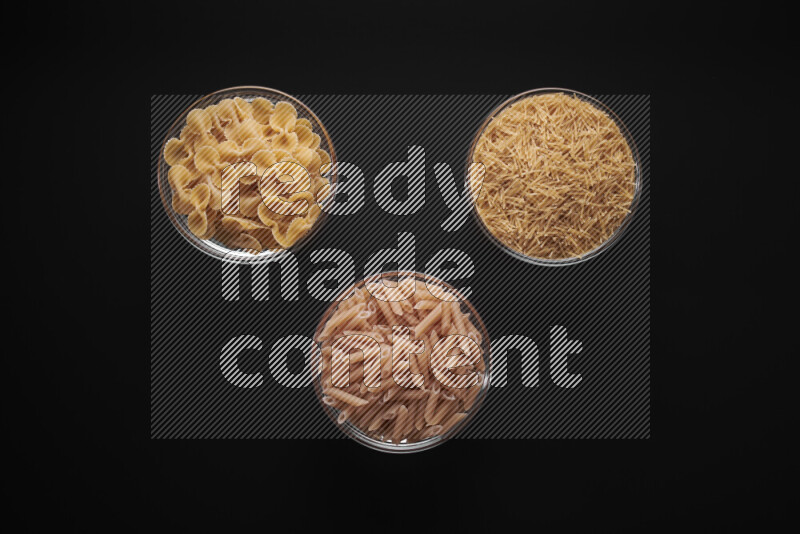 Different pasta types in glass bowls on black background