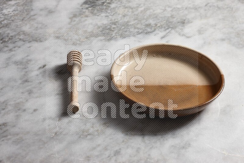 Multicolored pottery oven plate with wooden honey dipper on the side on grey marble background