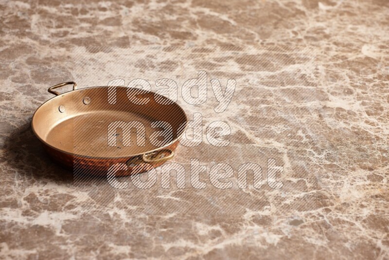 A small copper pan on beige marble background