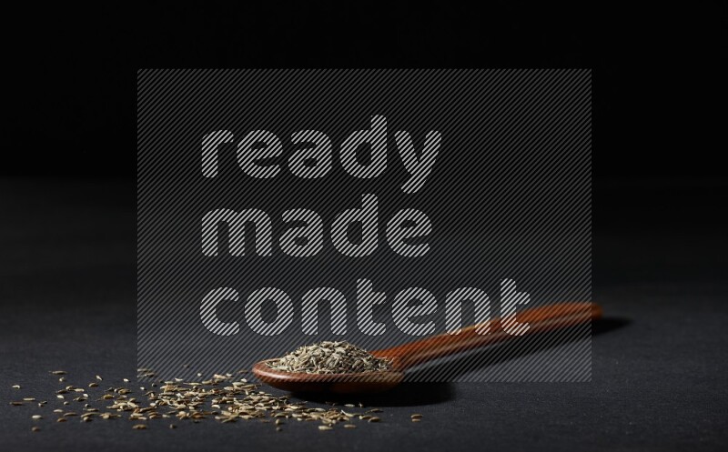 A wooden ladle full of cumin seeds on black flooring