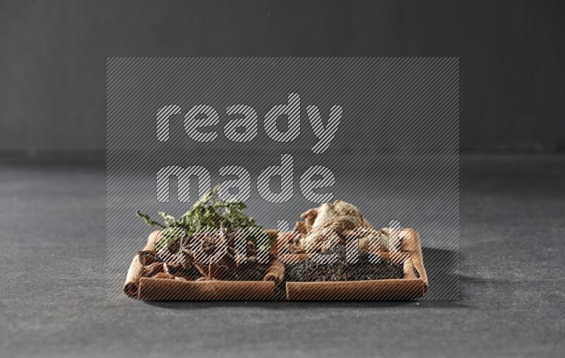 4 مربعات من عيدان القرفة ممتلئة بالشاي الأسود والزنجبيل المجفف والنعناع المجفف واليانسون النجمي على أرضية سوداء