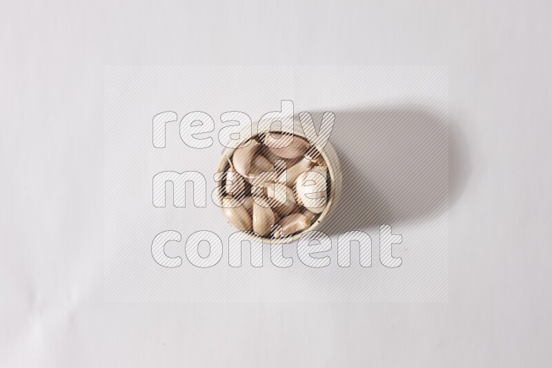 A beige pottery bowl full of garlic cloves on a white flooring