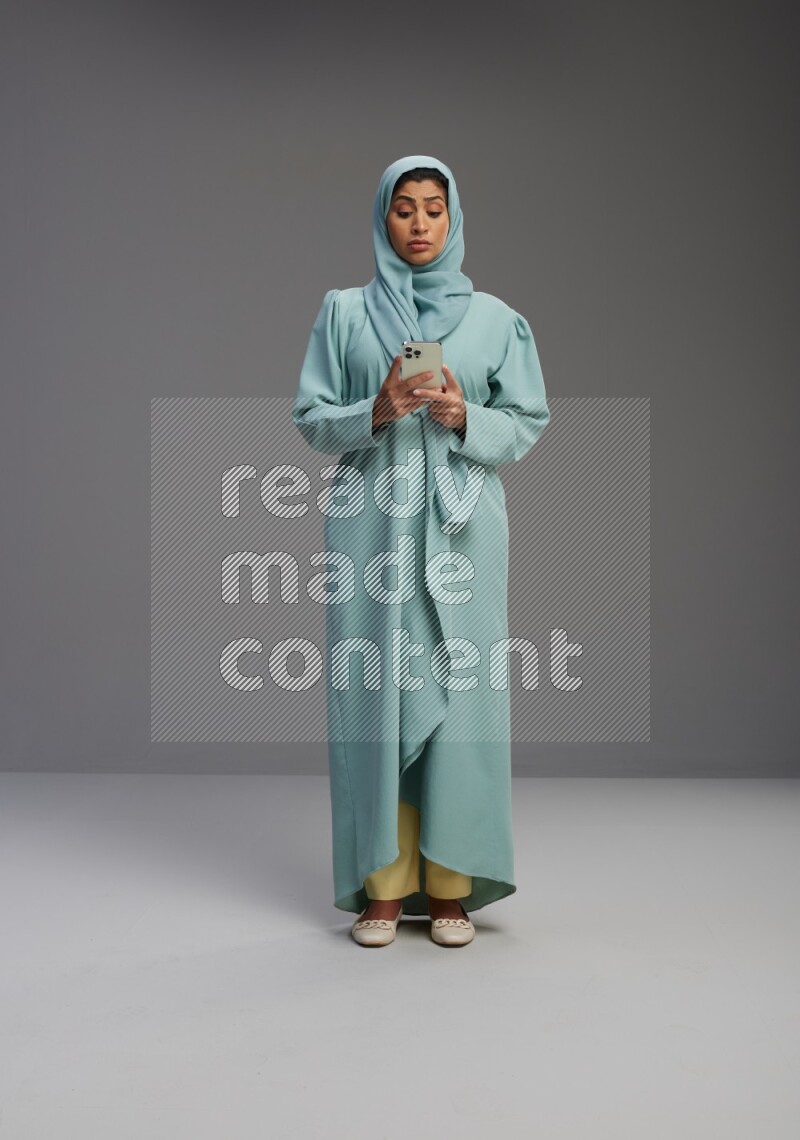 Saudi Woman wearing Abaya standing texting on phone on Gray background