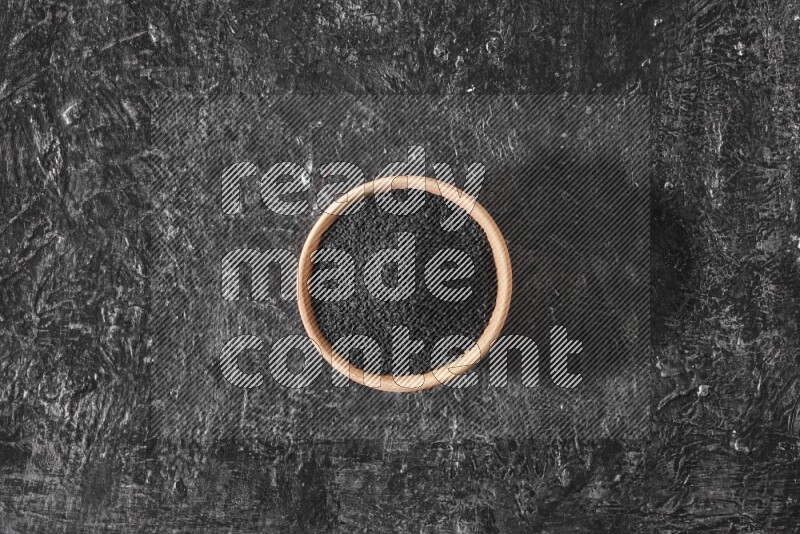 A wooden bowl full of black seeds on a textured black flooring