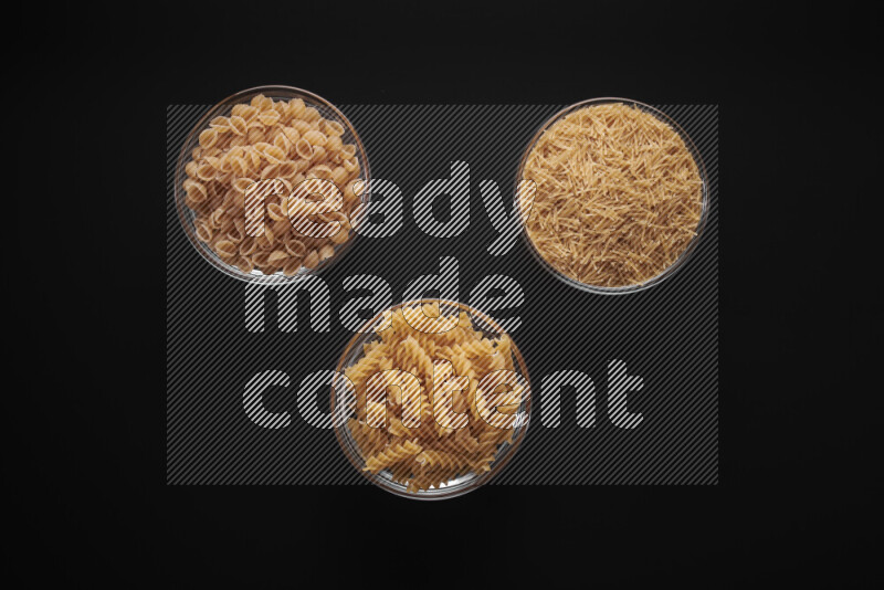 Different pasta types in glass bowls on black background