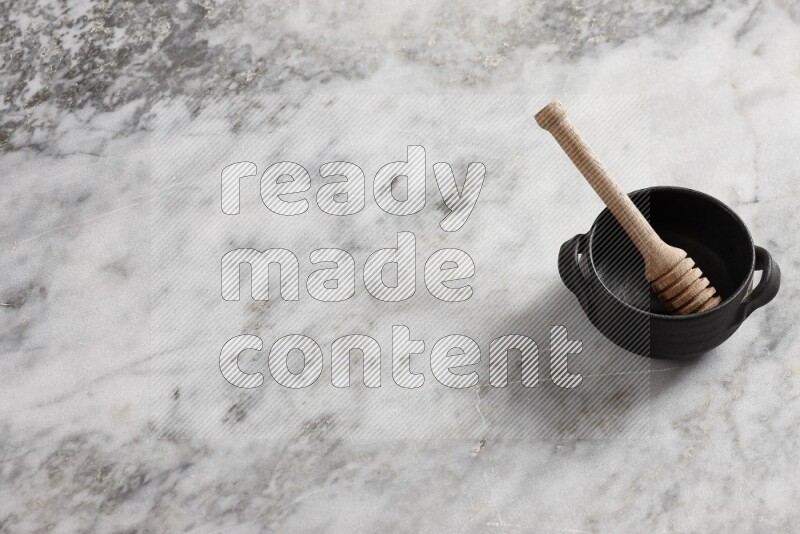 Black pottery bowl with wooden honey dipper in it on grey marble background
