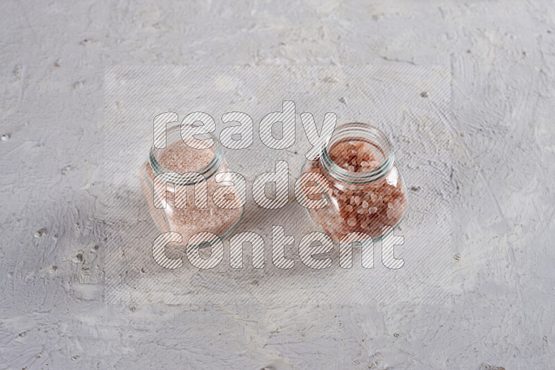 2 glass jars one is filled with fine himalayan salt and the other with coarse himalayan salt on white background