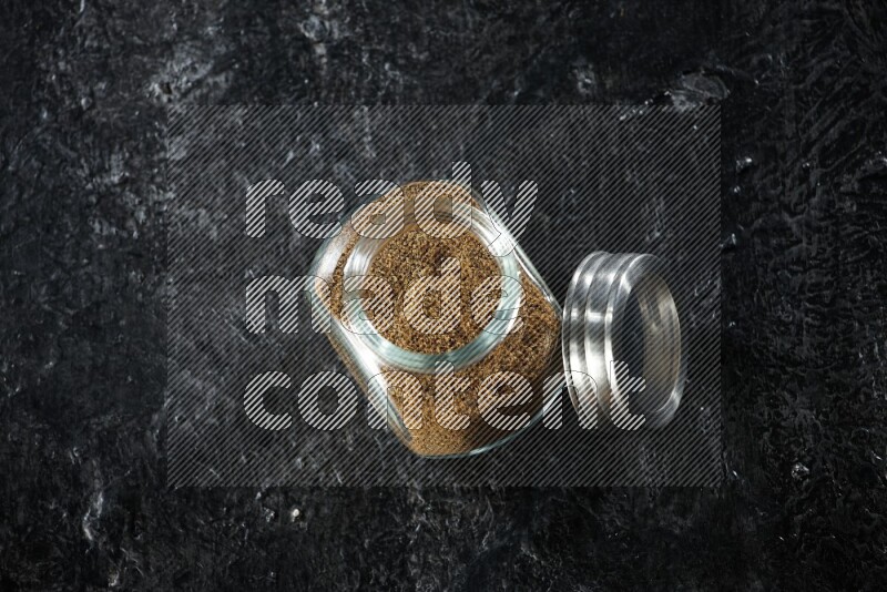 وعاء زجاجي للتوابل ممتلئ ببودرة الكمون على خلفية سوداء