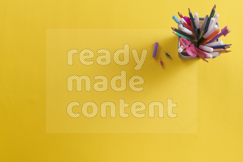 Pens, pencils and school supplies in a metal pen holder on yellow background