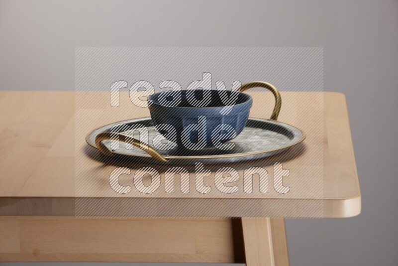 blue bowl placed on a rounded stainless steel metal tray with golden handels on the edge of wooden table