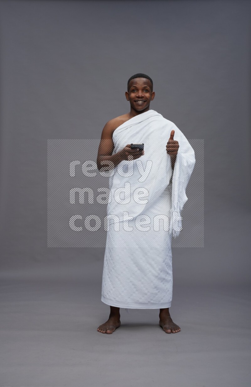 A man wearing Ehram Standing texting on phone on gray background