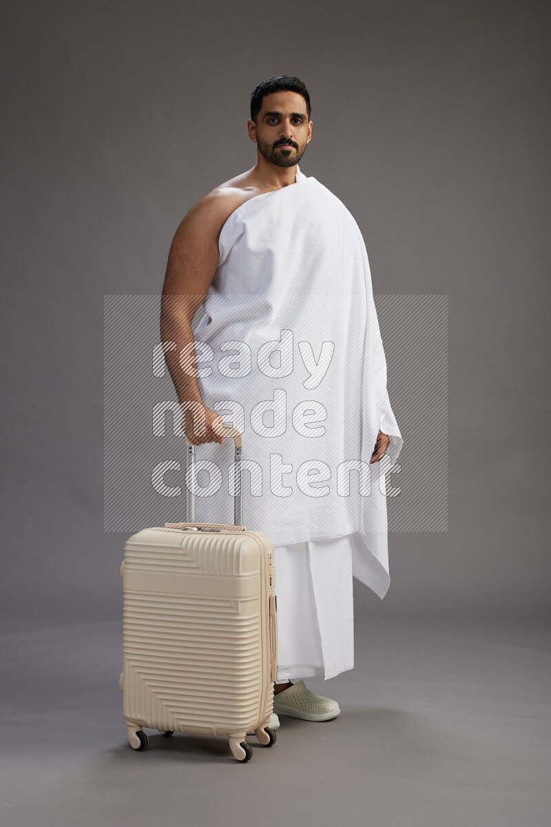 A man wearing Ehram Standing holding traveling bag on gray background