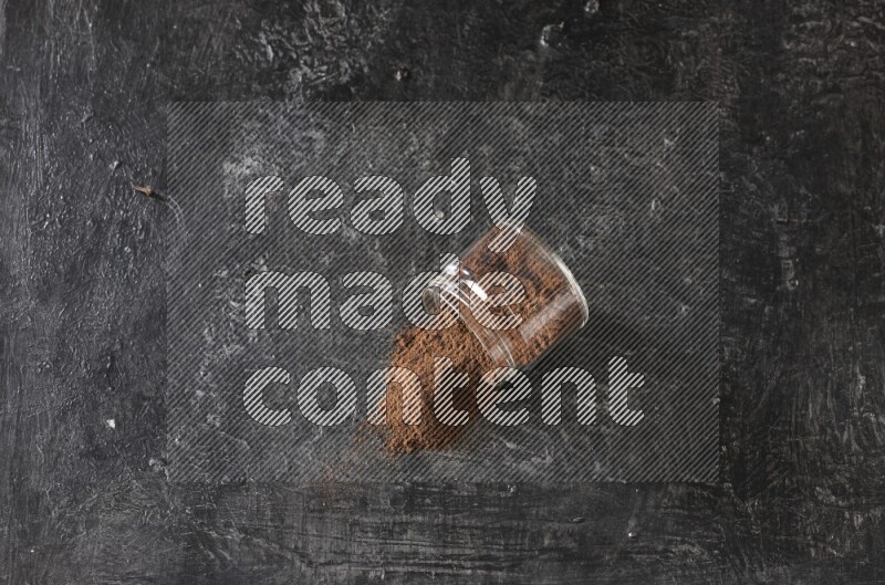 A flipped glass jar full of cloves powder on a textured black flooring
