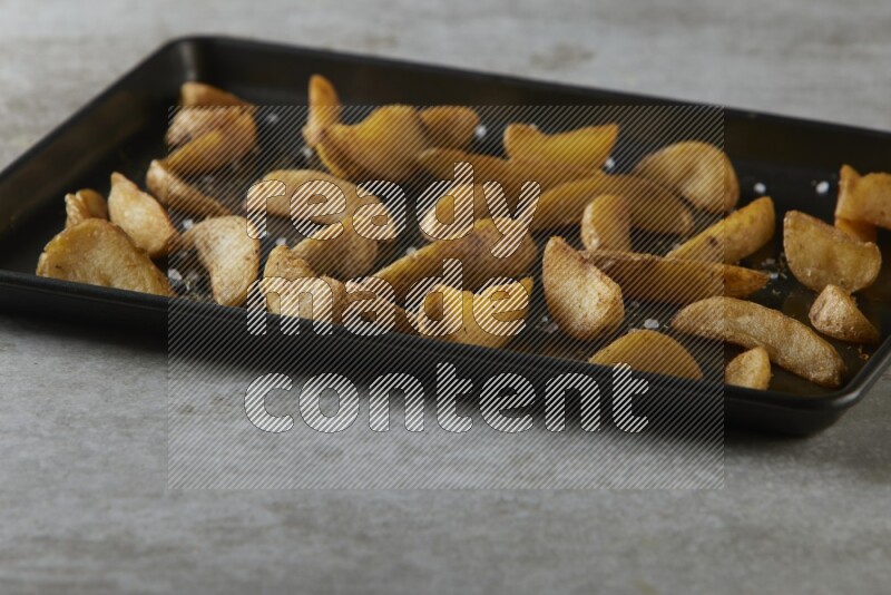 wedges potato in a black stainless steel rectangle tray on grey textured counter top