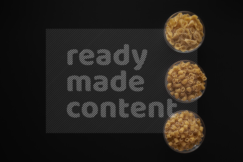 Different pasta types in 3 glass bowls on black background