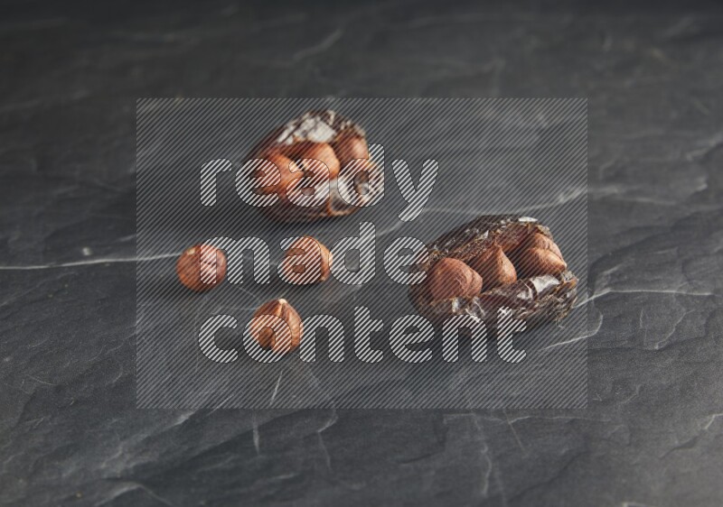 two hazelnuts stuffed madjoul dates on a black textured background