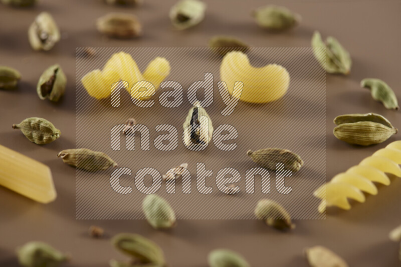 Raw pasta with different ingredients such as cherry tomatoes, garlic, onions, red chilis, black pepper, white pepper, bay laurel leaves, rosemary and cardamom on beige background
