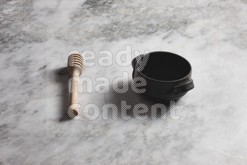 Black pottery bowl with wooden honey dipper on the side on grey marble background
