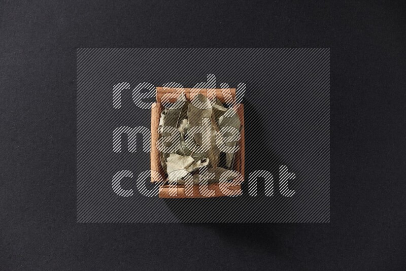 أربعة من أعواد القرفة مكونة شكل مربع بداخلها أوراق الغار علي خلفية سوداء