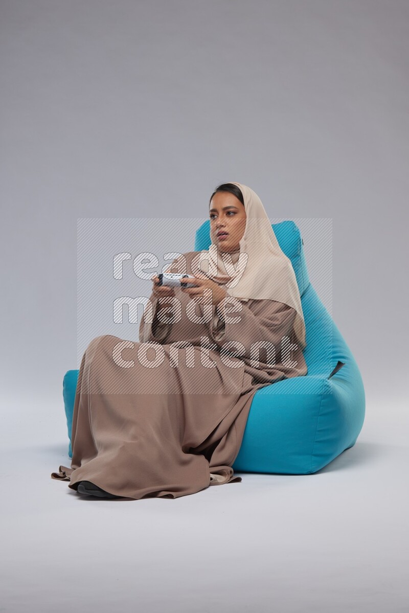 A Saudi woman sitting on a blue beanbag and gaming with joystick