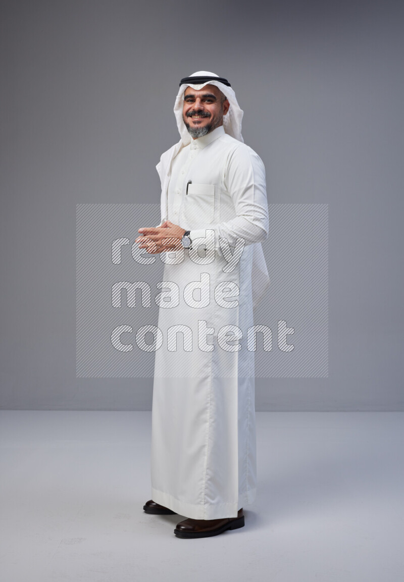 Saudi man Wearing Thob and white Shomag standing interacting with the camera on Gray background