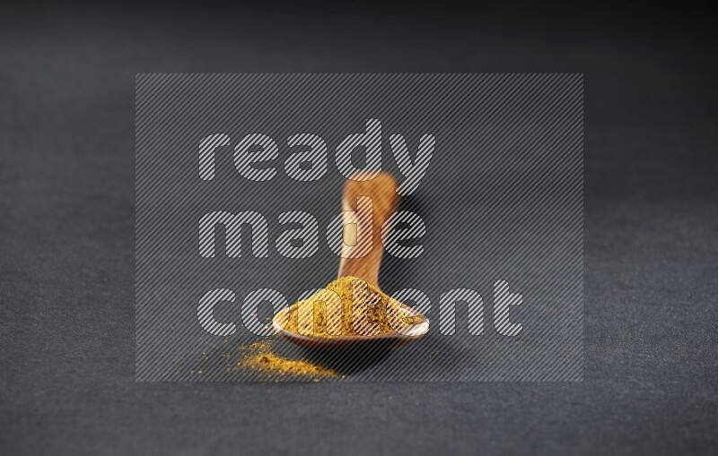 A wooden ladle full of turmeric powder on black flooring