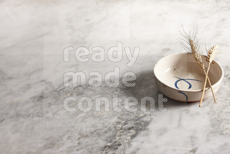 Wheat stalks on multicolored pottery bowl on grey marble background