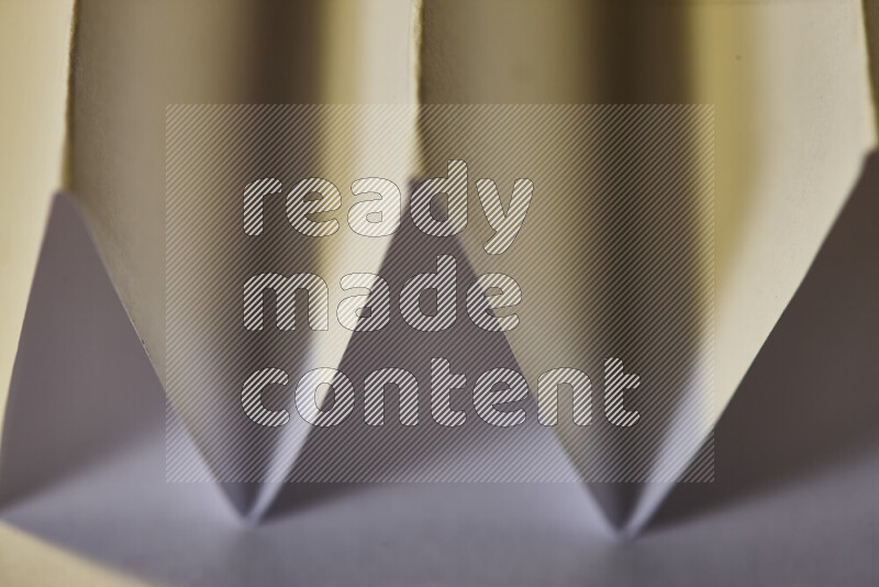 A close-up abstract image showing sharp geometric paper folds in white gradients and warm tones