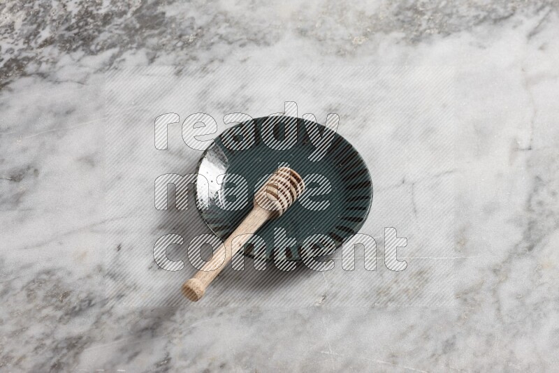 Multicolored pottery plate with wooden honey dipper in it on grey marble background