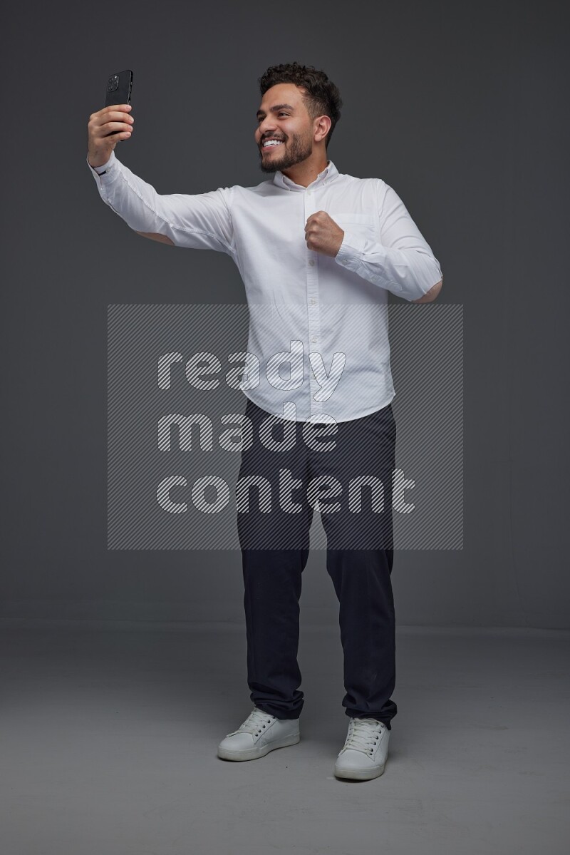 A man wearing smart casual and taking selfie with his phone eye level on a gray background