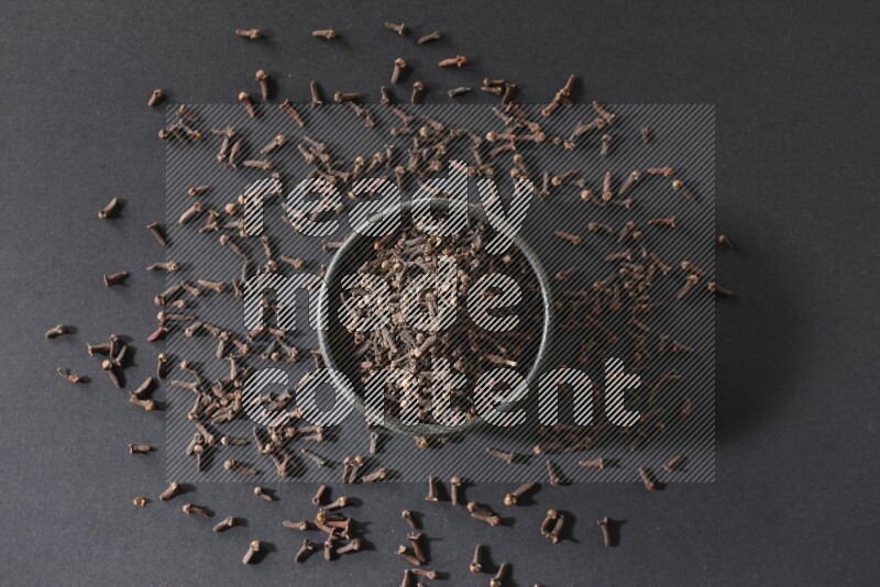 A black pottery bowl full of cloves on a black flooring