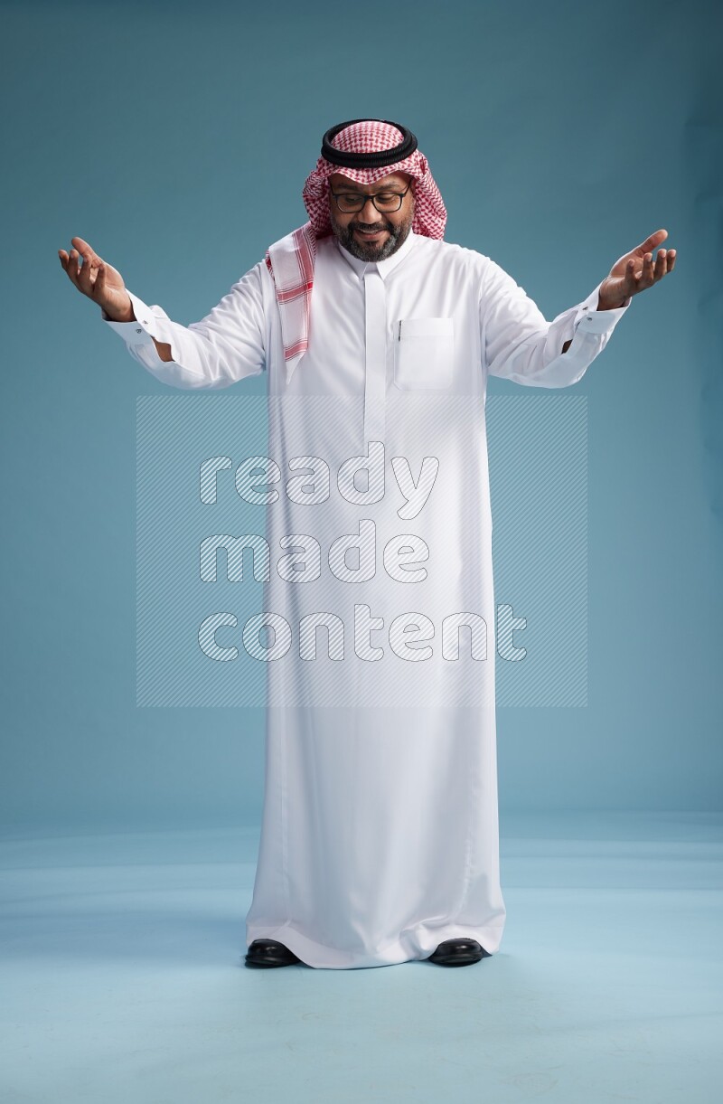 Saudi Man with shimag Standing Interacting with the camera on blue background