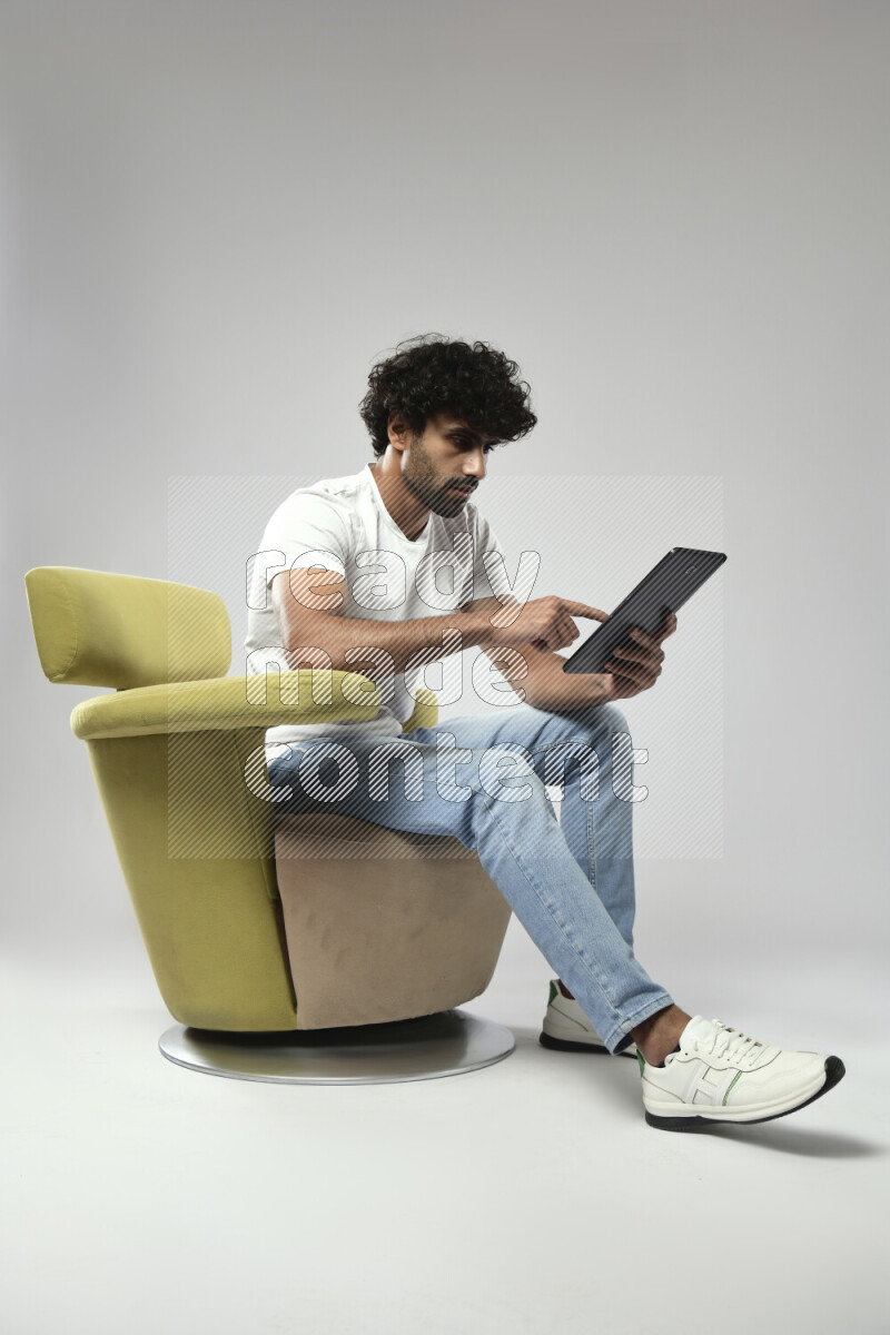 A man wearing casual sitting on a chair browsing on a tablet on white background