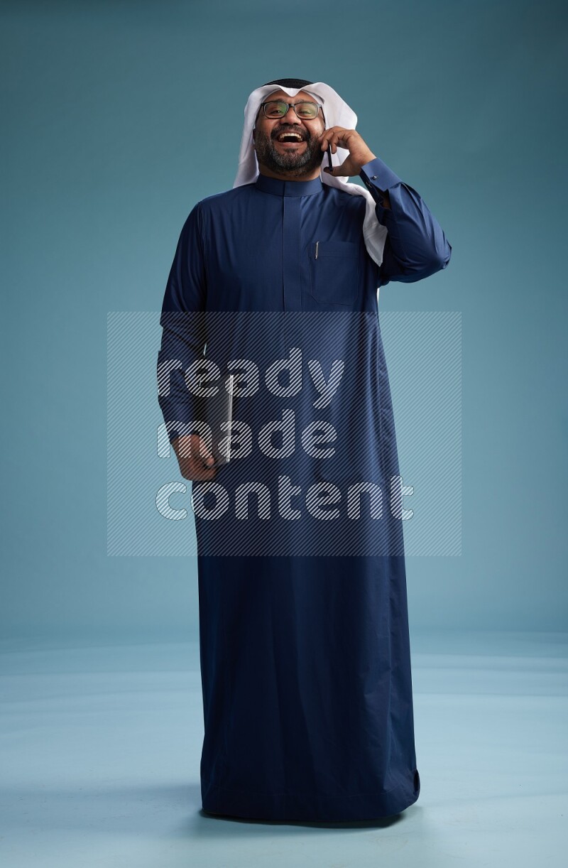 Saudi Man with shimag Standing talking on phone on blue background