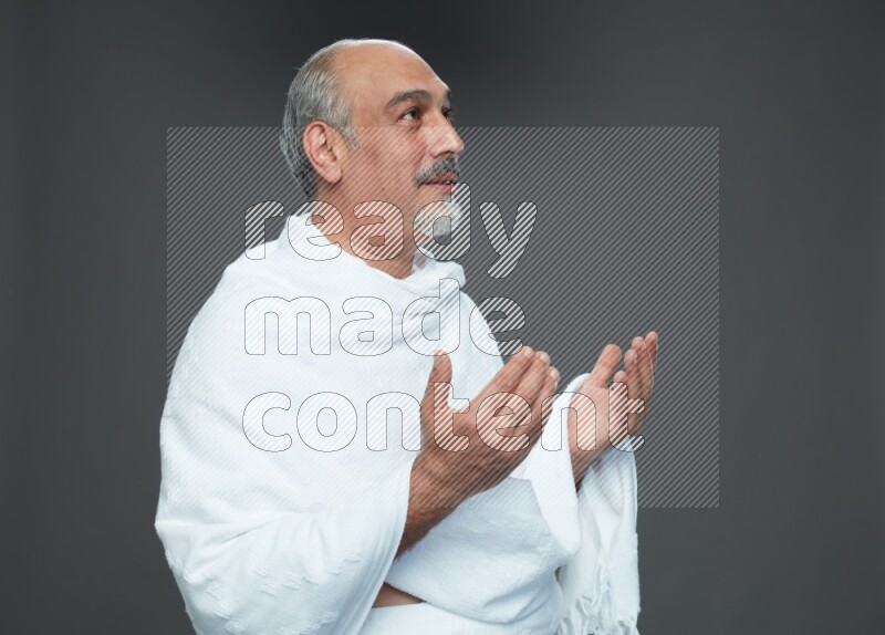 A man wearing Ehram Standing dua'a on gray background