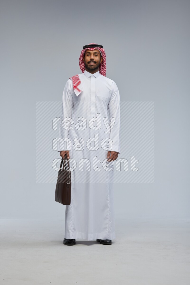Saudi man Wearing Thob and shomag standing holding bag on Gray background
