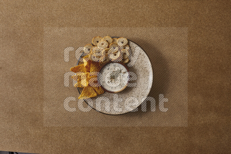 Assorted snacks on a pottery plate with a dipping on brown background