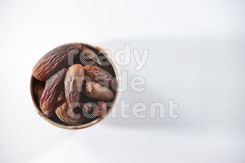 A beige ceramic bowl full of dried dates on a white background in different angles