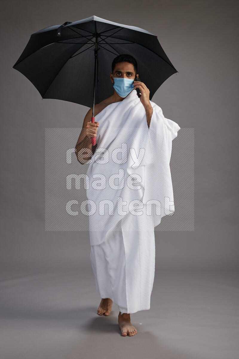 A man wearing Ehram and mask Standing holding umbrella on gray background on gray background