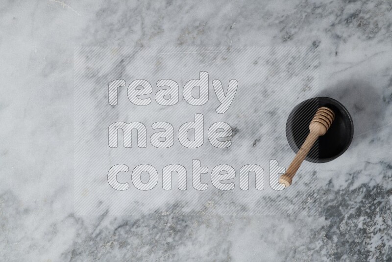 Black pottery bowl with wooden honey dipper in it on grey marble background