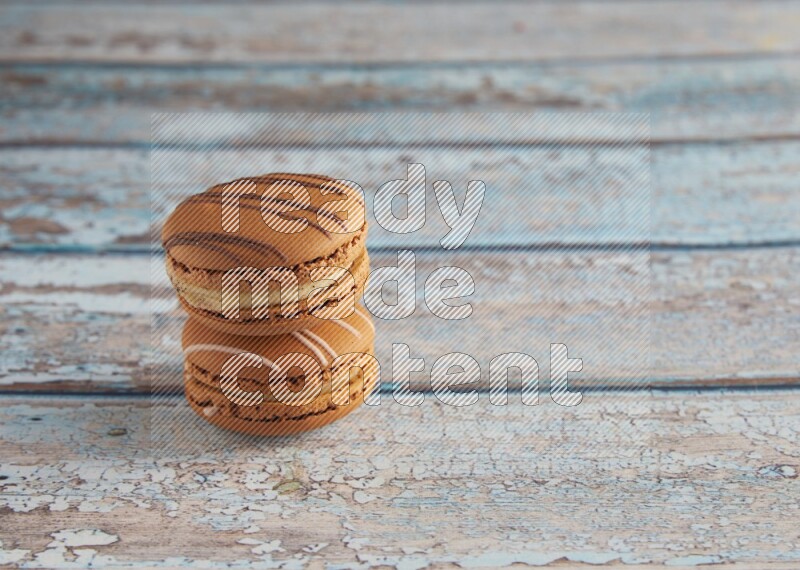 45º Shot of of two assorted Brown Irish Cream, and light brown Almond Cream macarons next to each other on light blue background