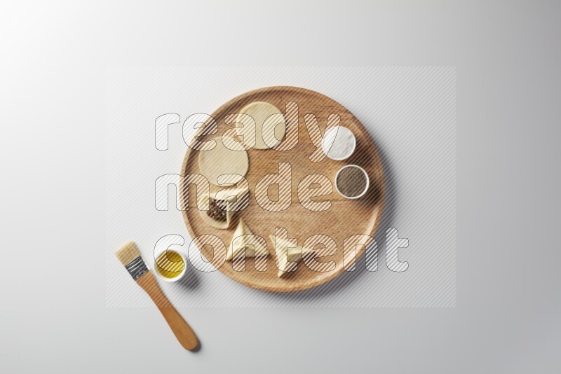 two closed sambosas and one open sambosa filled with meat while salt, black pepper and oil with oil brush aside in a wooden dish on a white background
