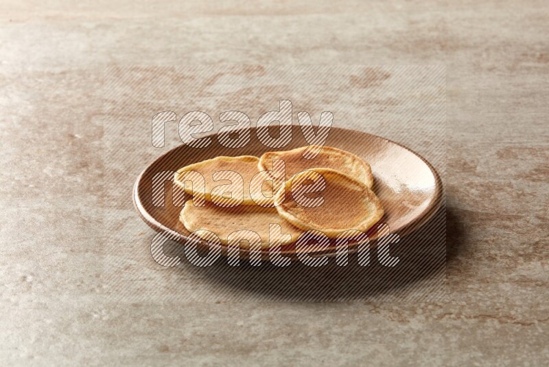 Four stacked plain mini pancakes in a brown plate on beige background